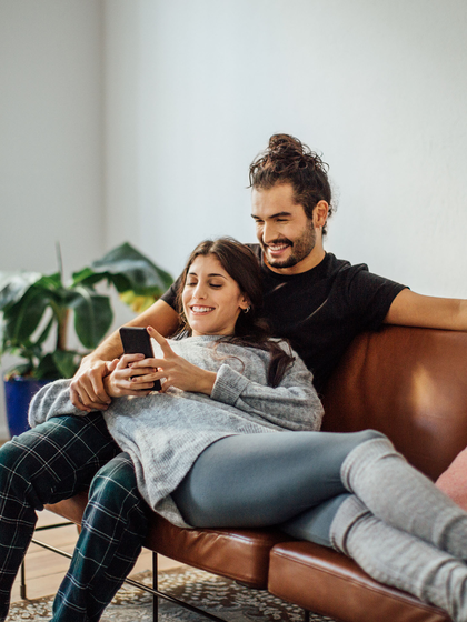 Happy young couple looking at a mobile phone while relaxing on sofa.