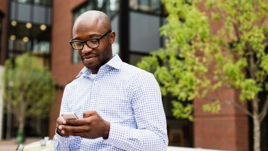 African American man wearing glasses and looking down at phone