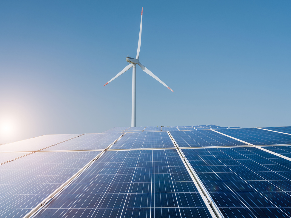 A wind turbine in the distance with a solar panel array in the foreground.