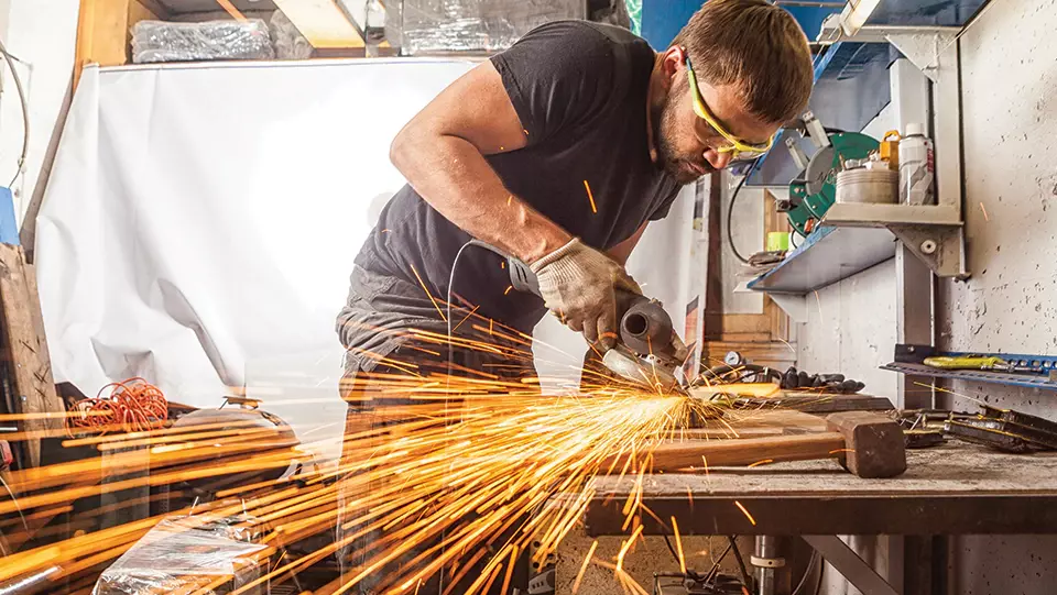 Worker in safety goggles using tool creating sparks and fire hazard.