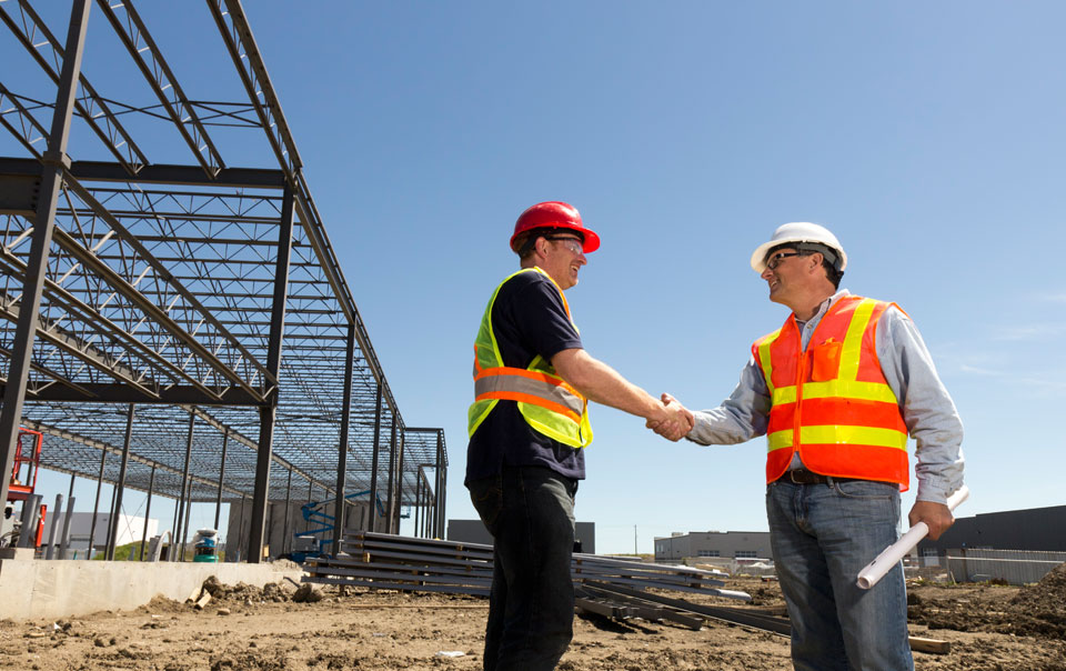 Contractor and subcontractor shake hands on a commercial construction site.