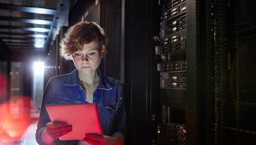Focused female IT technician using digital tablet in server room.