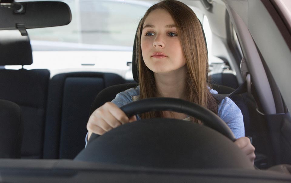 Teenage carefully driving behind the wheel of a car.