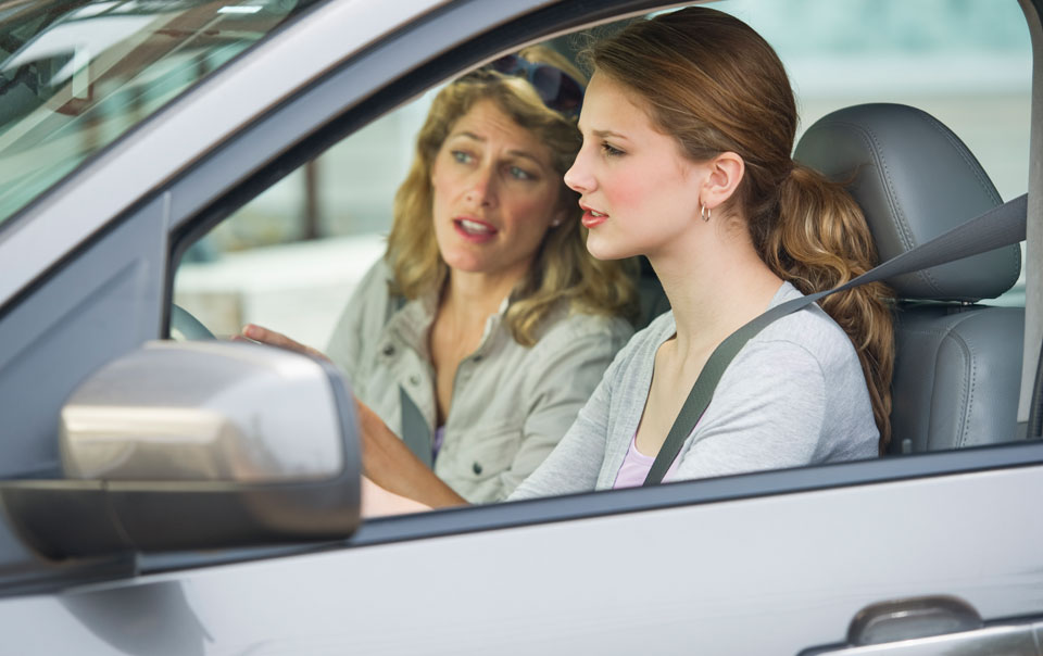 Parent teaching teen daughter how to drive.