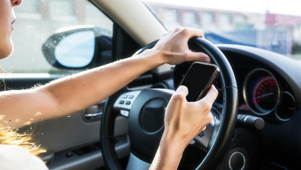 Woman texting on phone while driving behind the wheel.