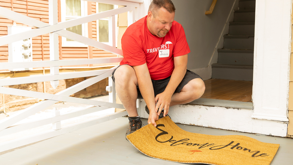 Man in front of window holding door mat.