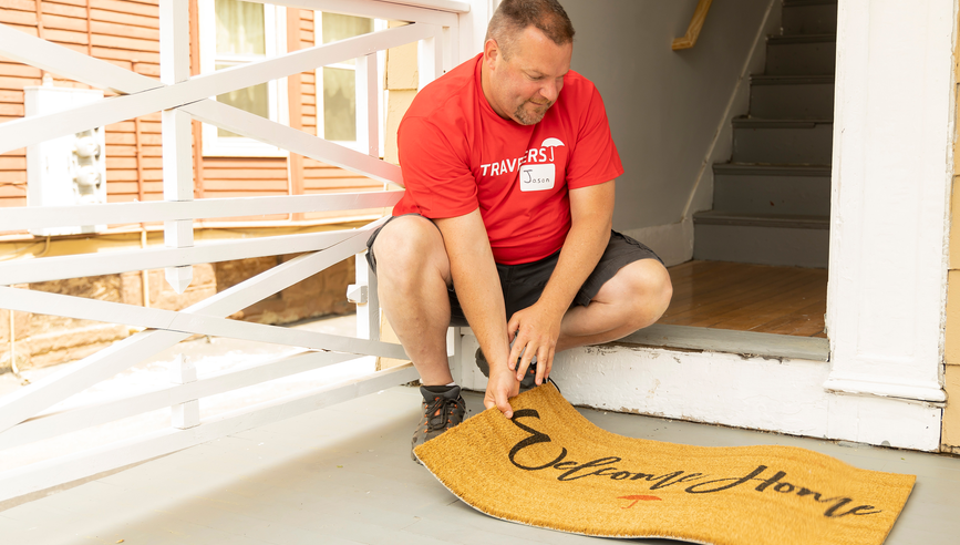 Man in front of window holding door mat.