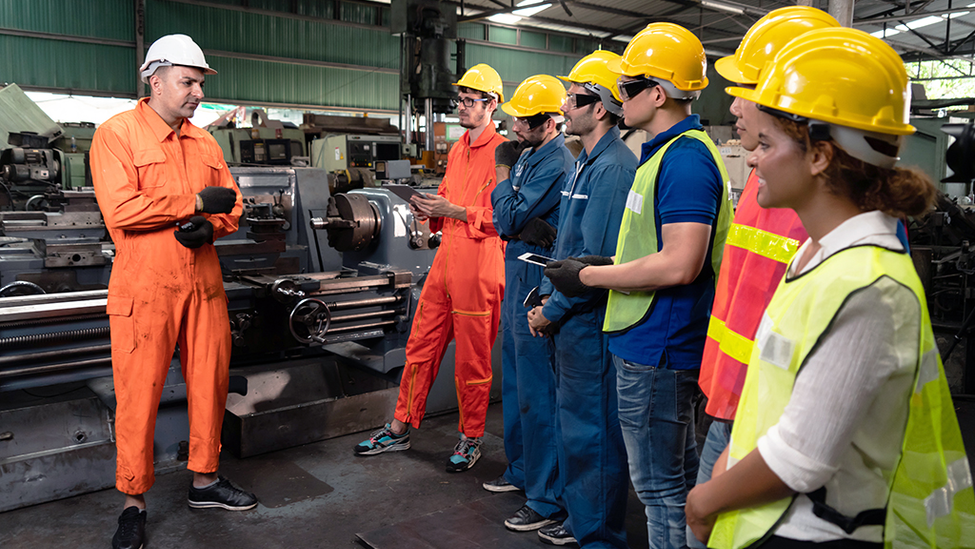 Workers wearing safety gear discussing workplace negligence in a manufacturing facility.