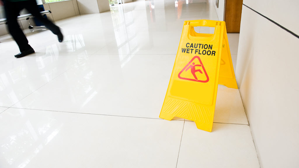 Yellow "caution wet floor" sign placed in hallway as a person walks nearby.
