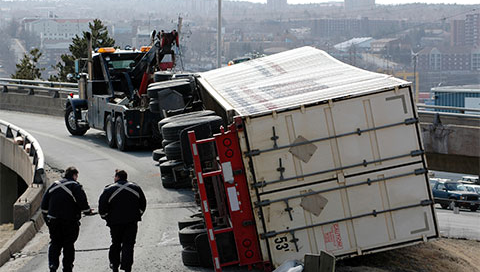 Overturned truck being pulled by tow truck.