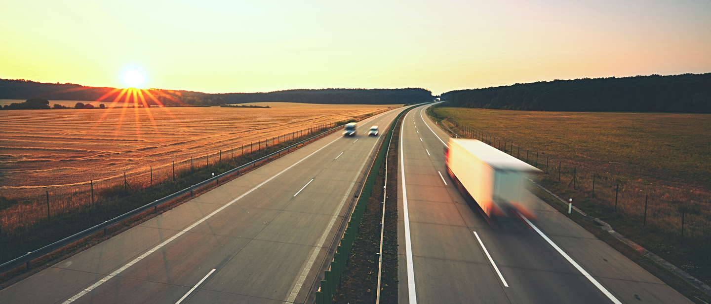 Long exposure shot of a rural highway with two cars traveling in one direction, while a semitruck travels away from the camera. 