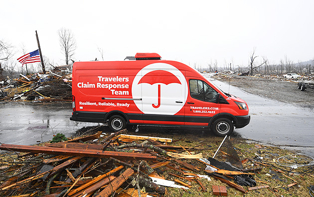 Red Travelers van with logo reading "Travelers Claim Response Team" at the site of a storm.