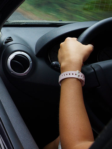 A rear view mirror is seen as person drives down the road with an open window.