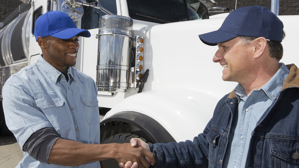 Two truck drivers wearing blue baseball caps shake hands