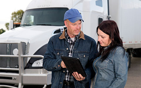 Truck driver stands beside woman while pointing to tablet device