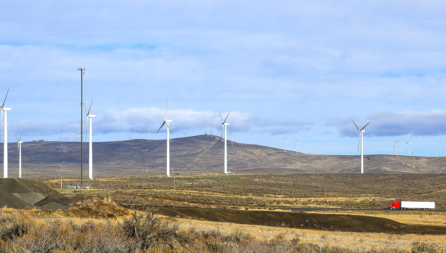 A truck driving next to wind turbines.