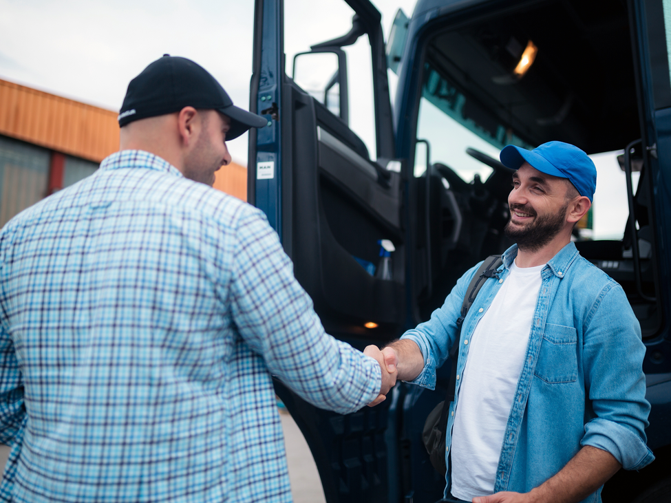 A trucker shaking hands with another man and smiling.