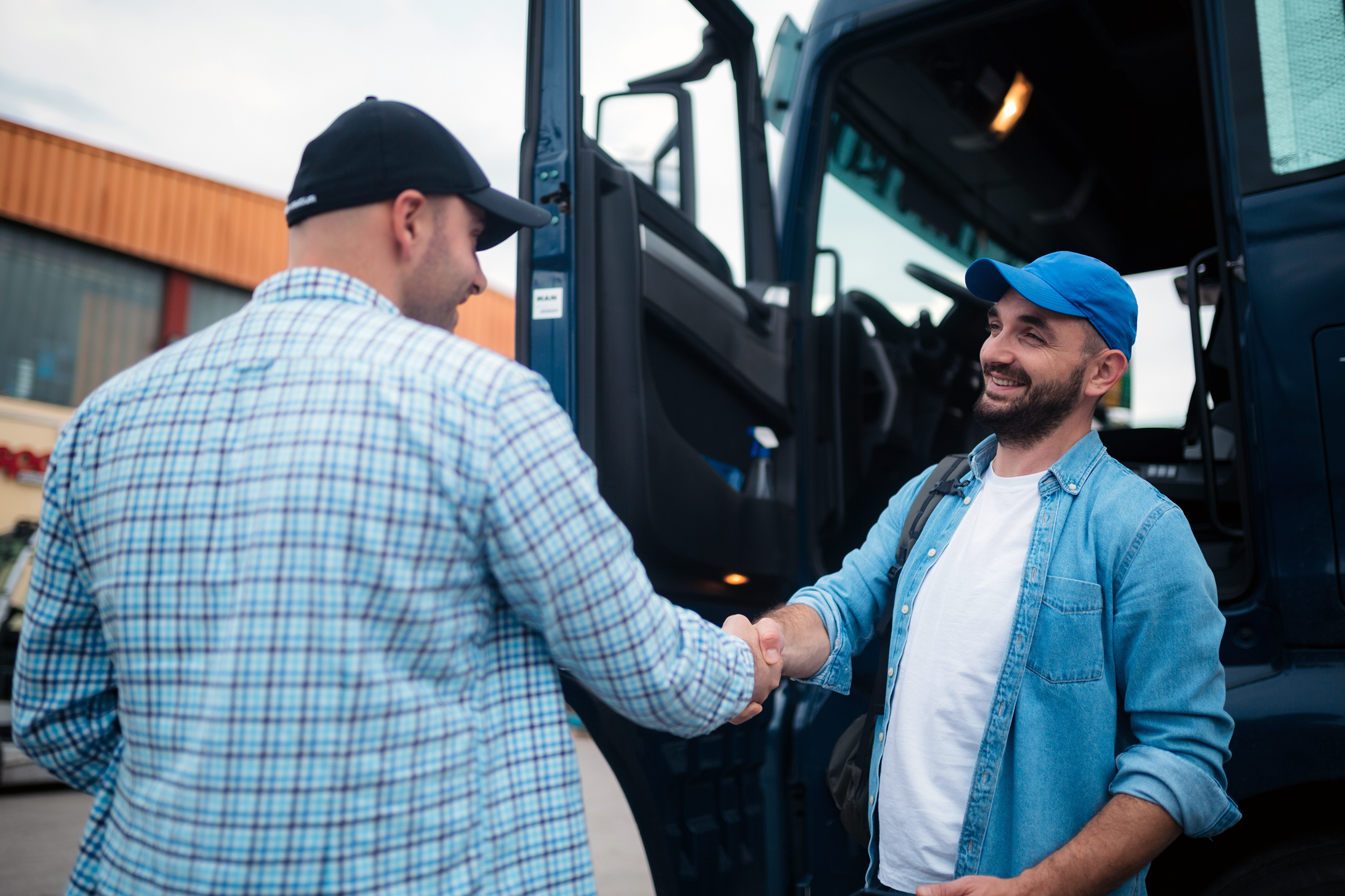 A trucker shaking hands with another man and smiling.