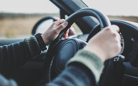 Man driving a car with two hands on the steering wheel.