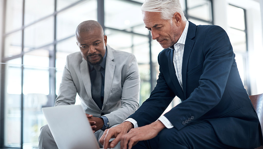 Two senior business managers meeting outside of an office, looking at a laptop computer 