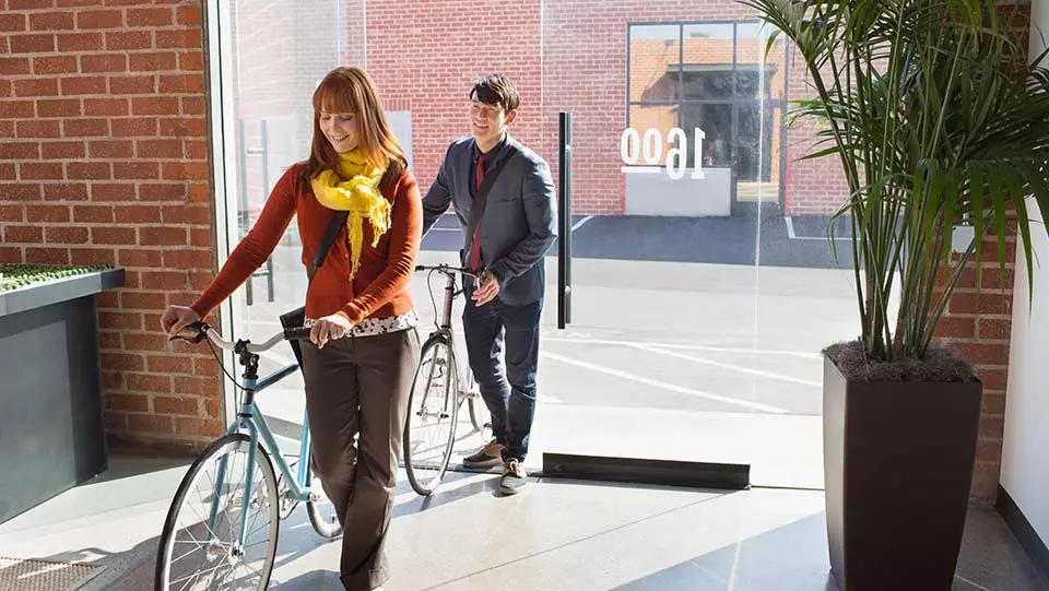 Two people walking into office with bikes.