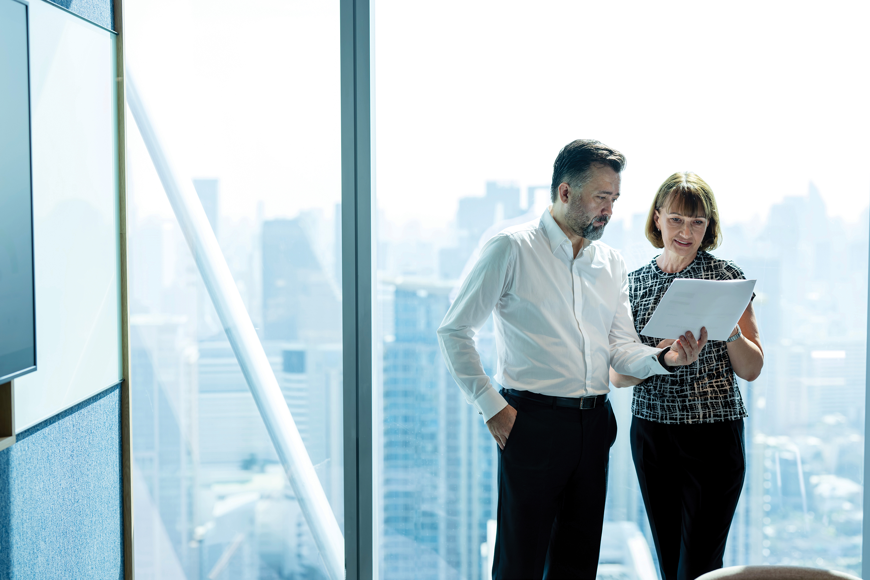 Two professionals discussing a paperwork in an office building next to the windows.