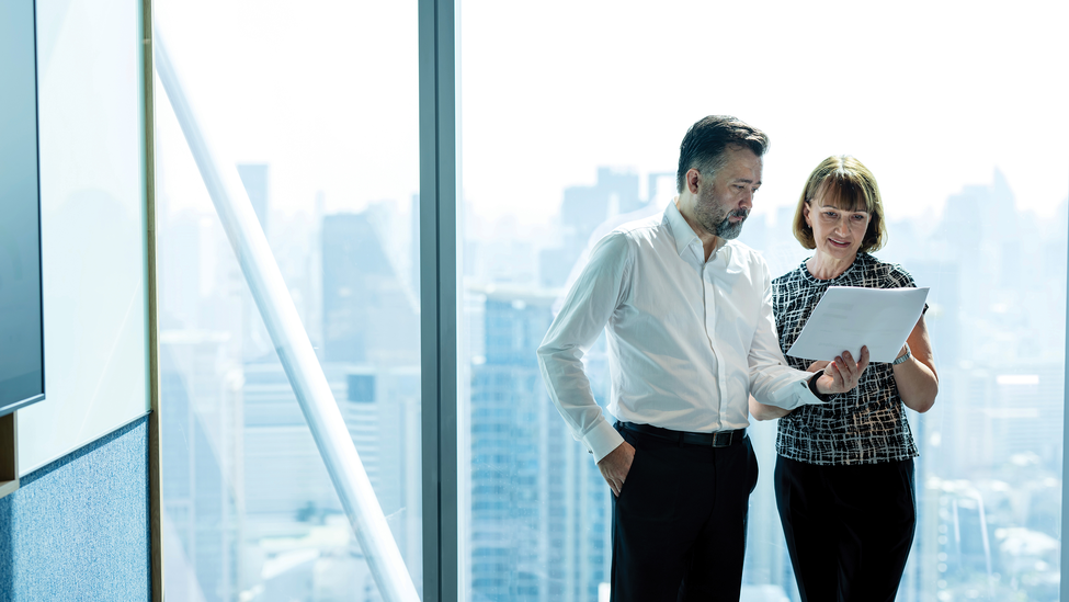 Two professionals discussing a paperwork in an office building next to the windows.