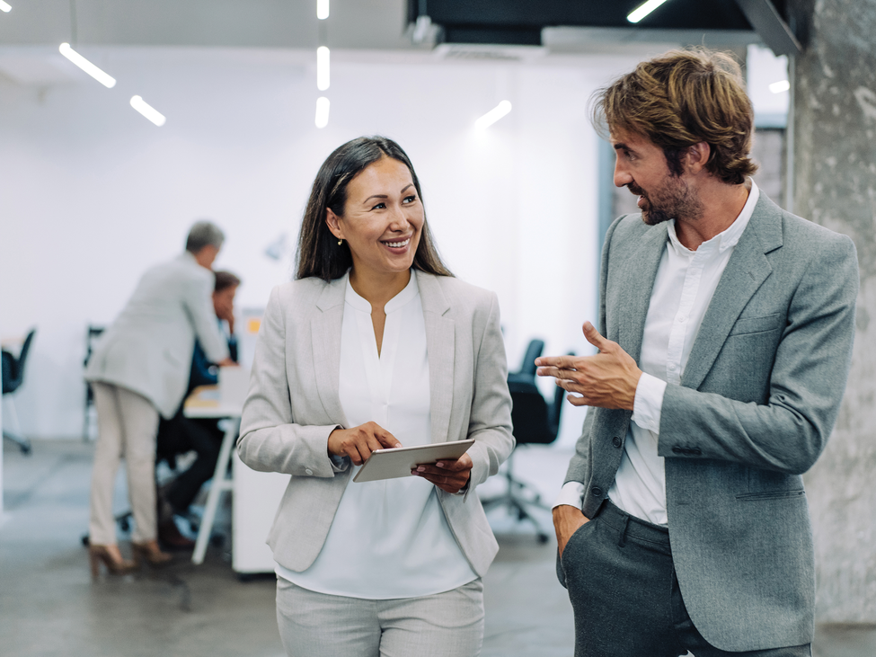 Two business professionals walking and talking to each other in an office.