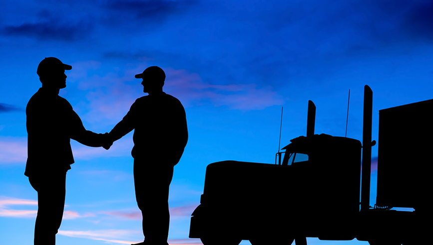 Two male truckers' shaking hands at dawn. The sky are of blue and purple hues.