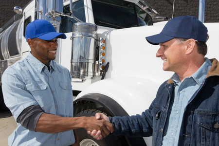 Two truck drivers wearing blue baseball caps shake hands