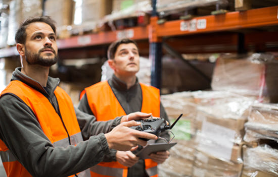 Two workers in warehouse using drone.