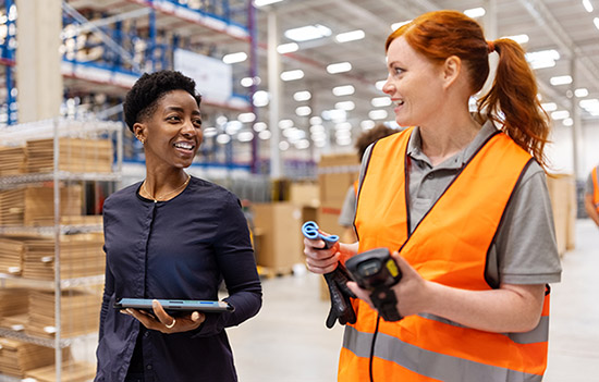 Two employees walking in a warehouse, having a discussion.