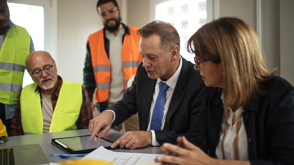 A group of people who work in the construction industry having a meeting, looking at plan and a digital tablet on a desk.