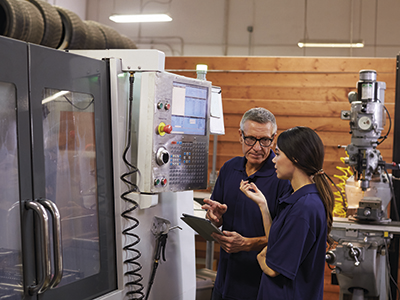 An engineer training his apprentice to use a CNC machine.