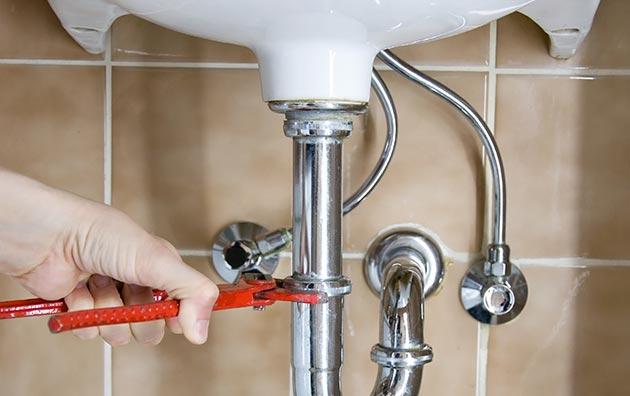 Person tightening sink pipes to prevent water damage in home.