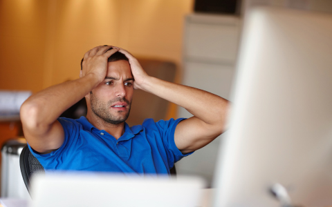 man sitting at a desk, holding his hands to his head in exasperation