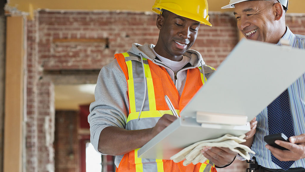 Two contractors reviewing a contractual document in hard hats.