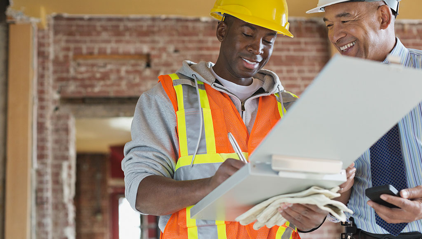 Two contractors reviewing a contractual document in hard hats.