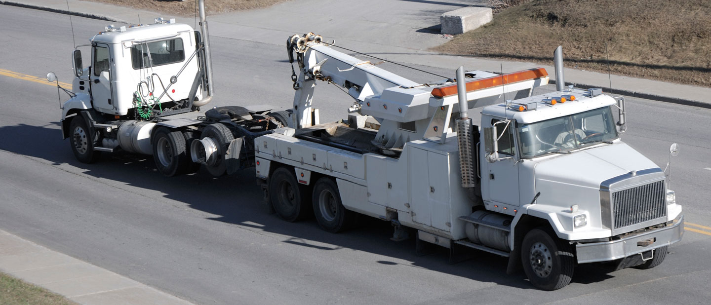 White semitruck being towed by a large white tow truck.