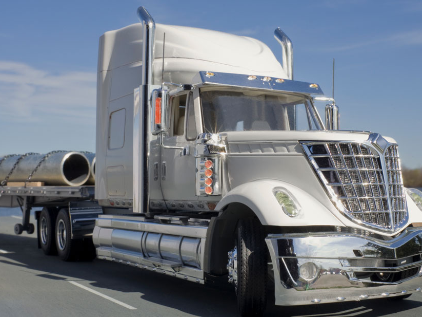 White truck hauling metal cargo on a remote road.