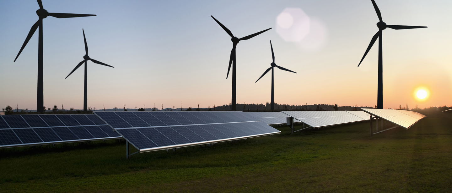 Landscape view of solar farm at sunset, with wind turbines in the background.