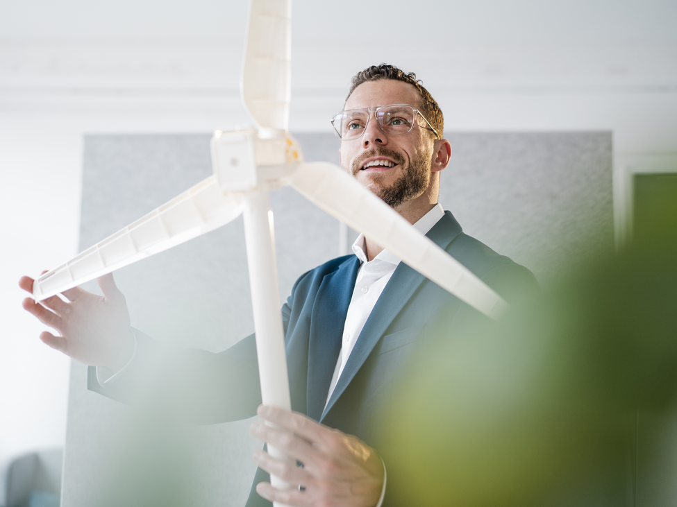 Smiling businessman touches the blade of a windmill model.