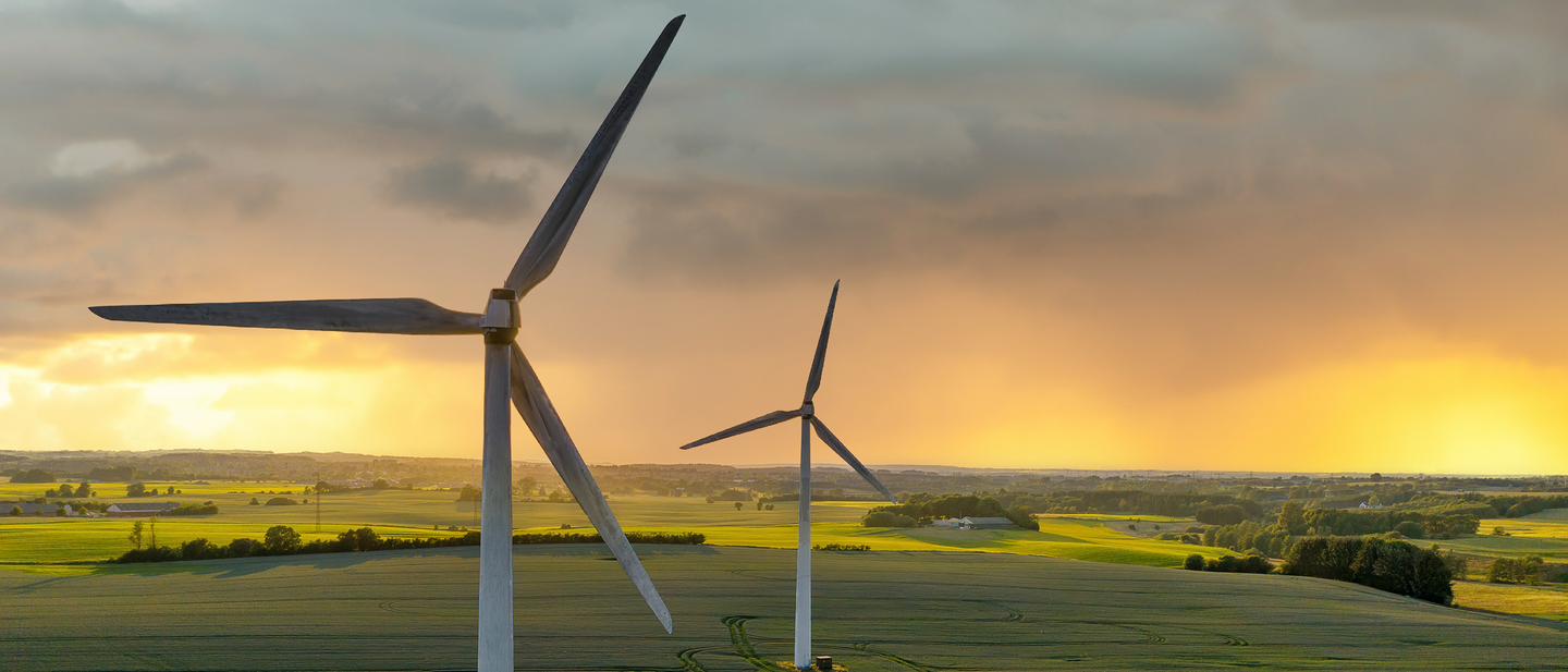 Two wind turbines in an open landscape with mountains in the far distance.