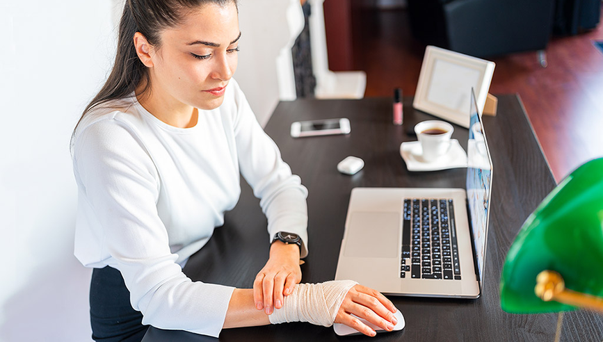 An office worker sitting at her desk, with a bandaged arm.