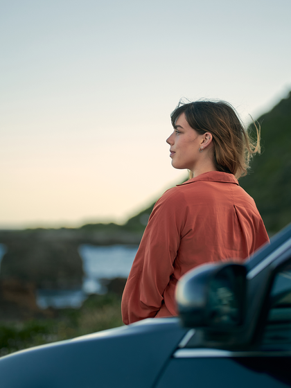 Woman looking out at the beach by her SUV.