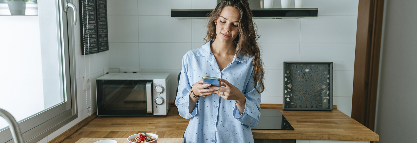 woman standing in her kitchen on her phone, Mobile & Web Expriences