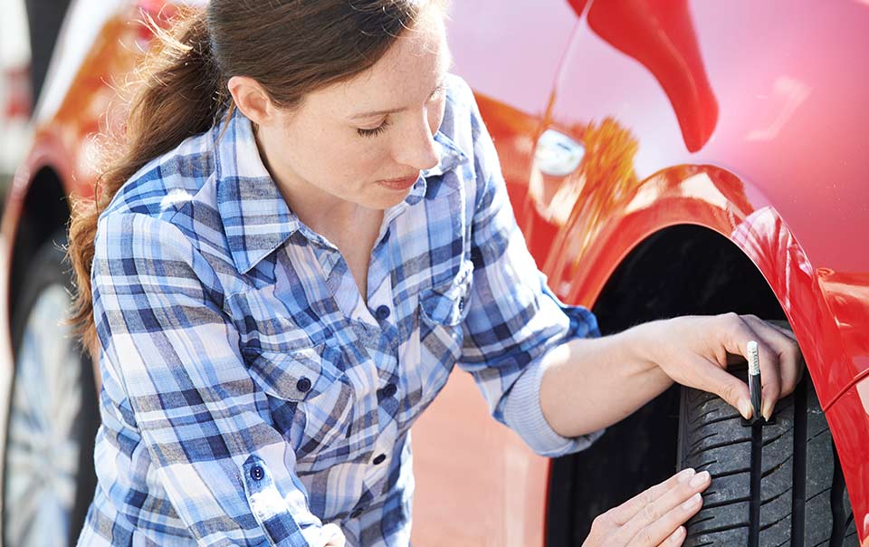 Woman checking tire tread of car as part of regular car maintenance routine.