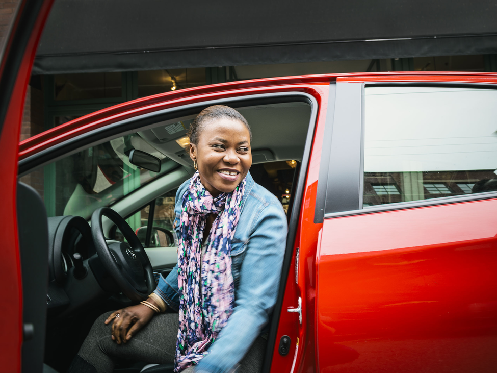 Smiling woman in driver’s seat opening door and talking to someone.