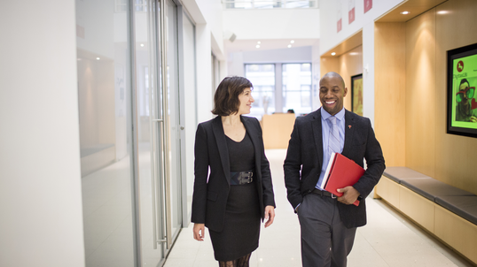 Travelers agents walking down an office hall with a red folder.