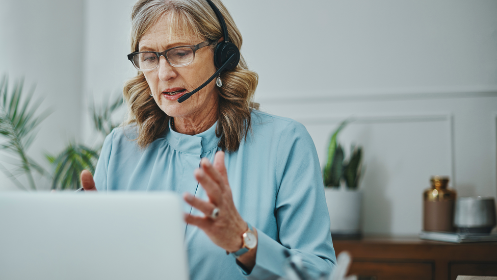 Shot of a mature woman using a headset and laptop in a modern office